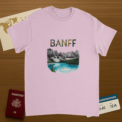 light pink Banff Canada Unisex Travel T-Shirt on wooden background with world map, passport, and boarding pass